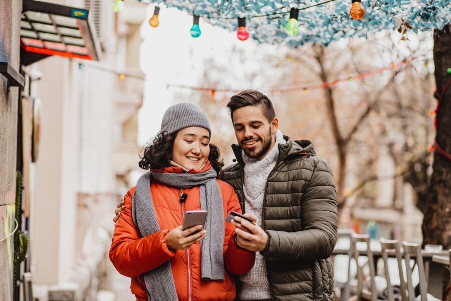 A couple outdoors using credit card and mobile phone to pay for holiday shopping.