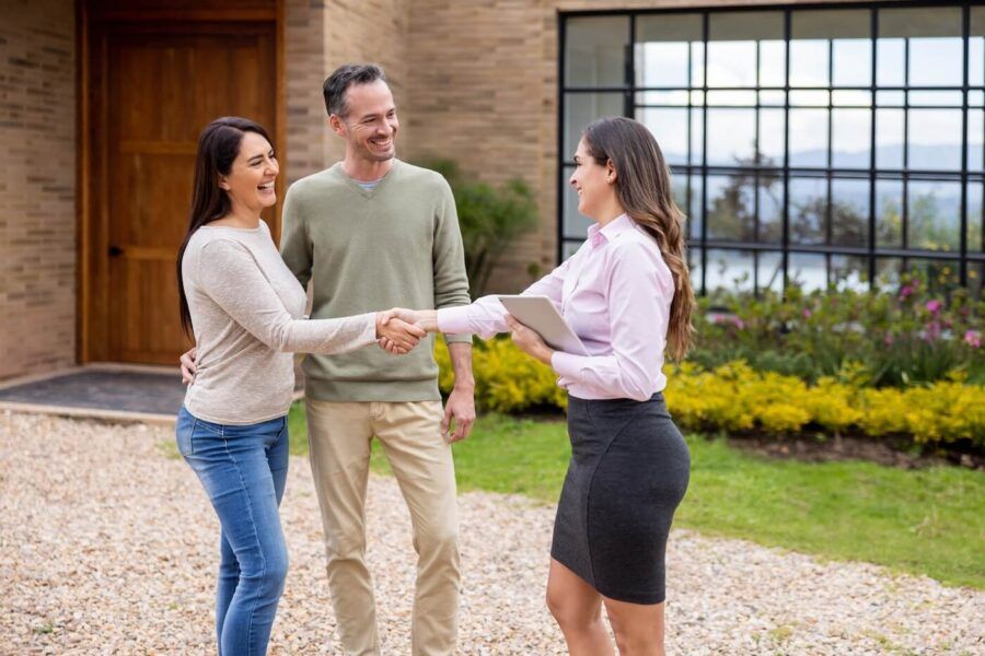 Happy couple shaking hands with a female real estate agent next to their new house