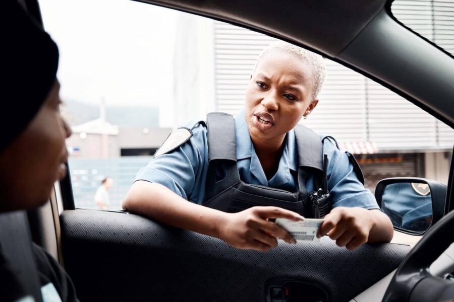Concerned policewoman speaking with a female driver at the roadside while holding her driver's license