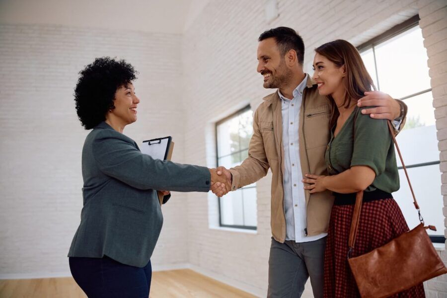 A smiling female real estate agent shaking hands with a couple who just purchased a new home