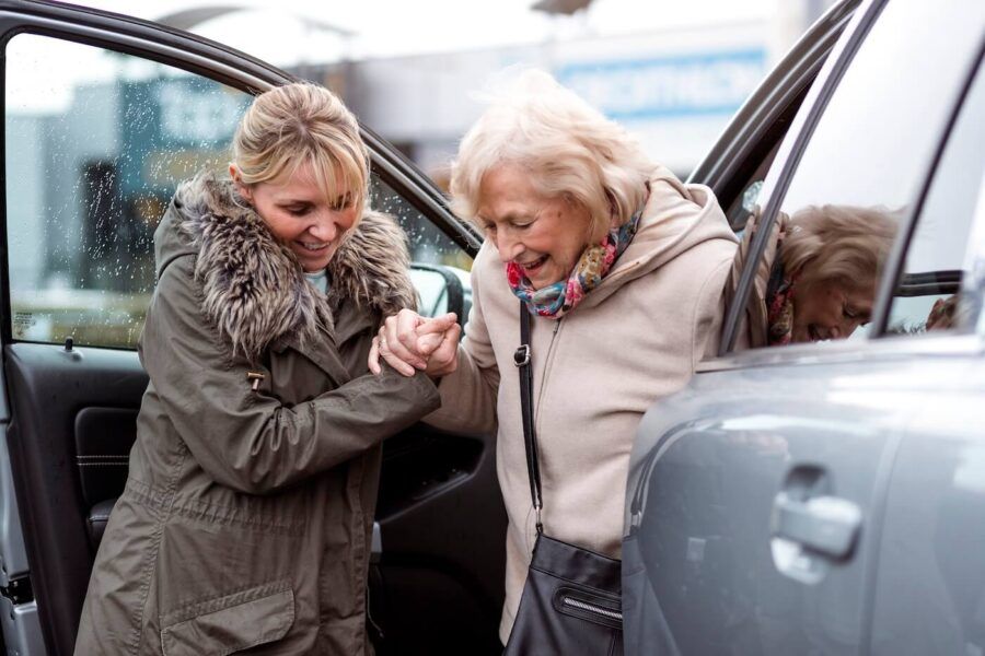 Smiling woman helping a senior lady to get out of the car in winter