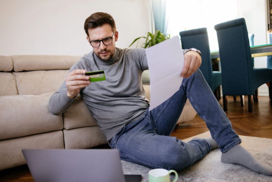 Mid adult man considering paying bills online at home using credit card and laptop