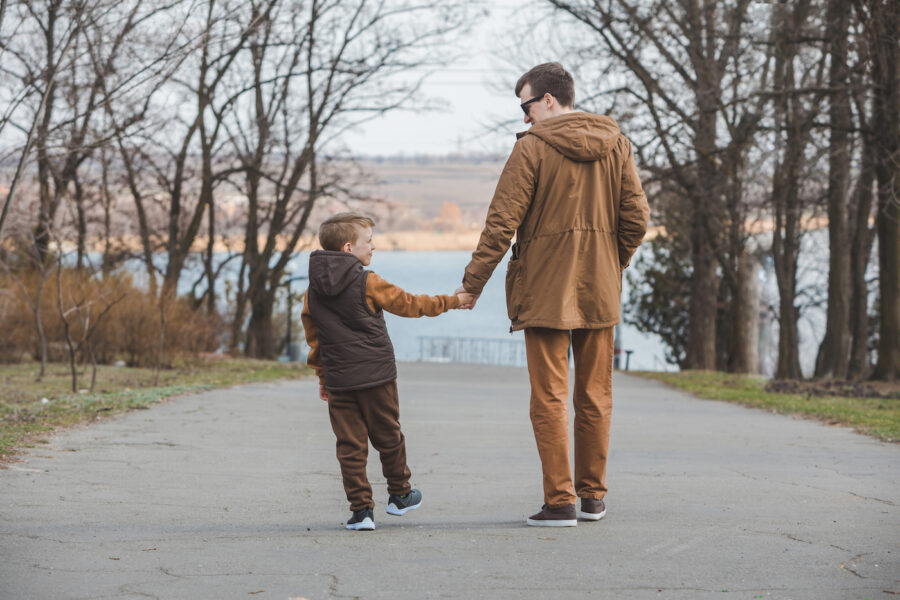 father with son walking by park holding hands