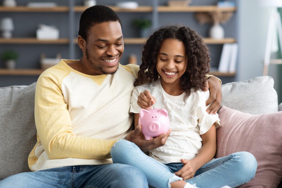 Black girl and father putting coins into piggy bank, representing a 529 account