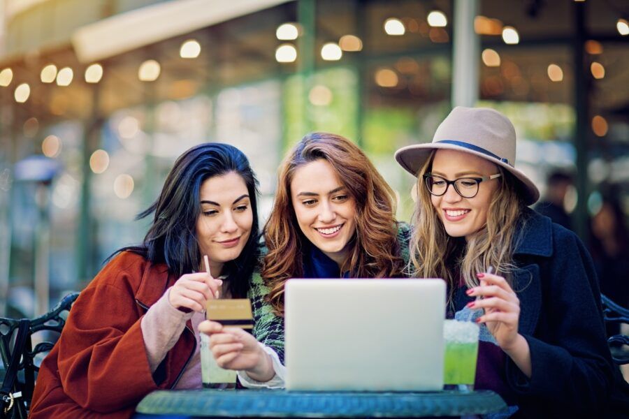 Three women looking at a laptop. One in the center is holding a credit card.