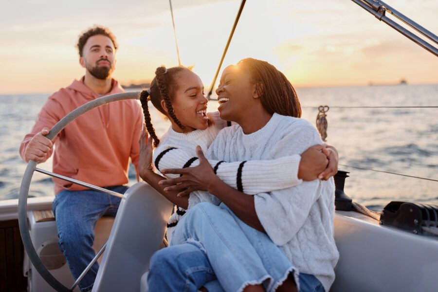 Father sailing the yacht while mother and daughter embrace and enjoy the view. Luxury vacation at sea.