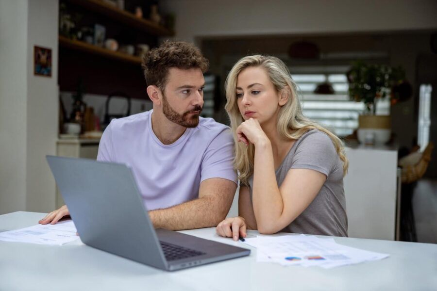 Concerned young couple reviewing their finances at home with an open laptop beside them