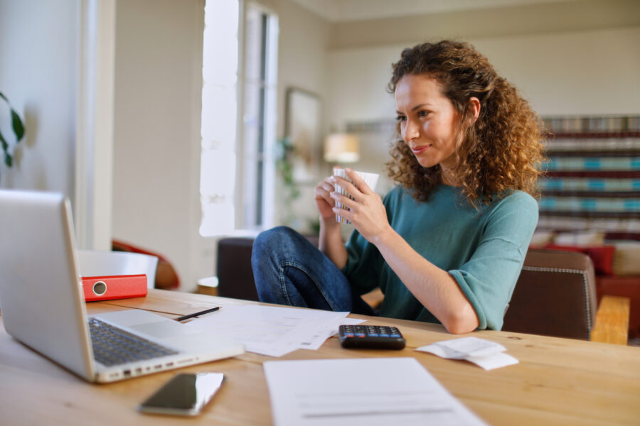 A first-time homeowner confidently staring at her online taxes on her laptop while holding a mug.