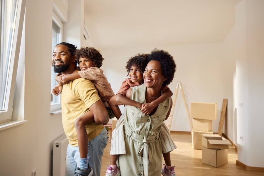 Happy family of four in their new living room surrounded by moving boxes, the parents are holding their young kids