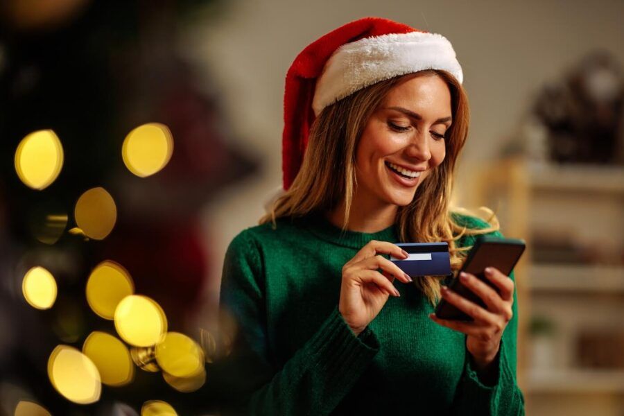 A smiling woman in Santa's hat is buying presents online with her credit card