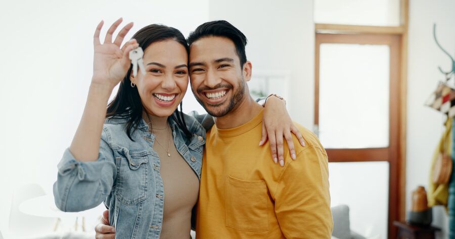 A smiling couple embracing and holding the keys to their new home.