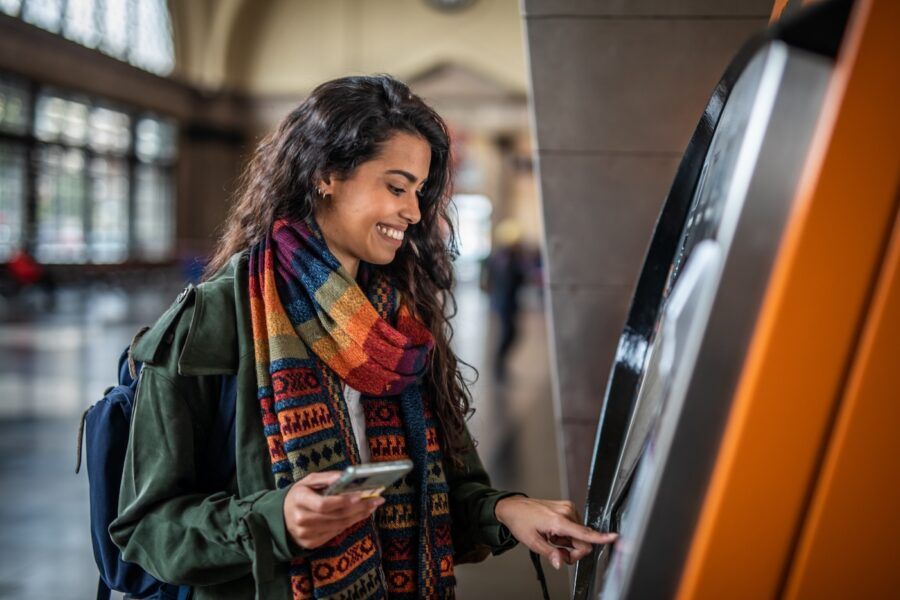 A casually dressed young woman using an ATM in a metro station in Barcelona to withdraw her money.