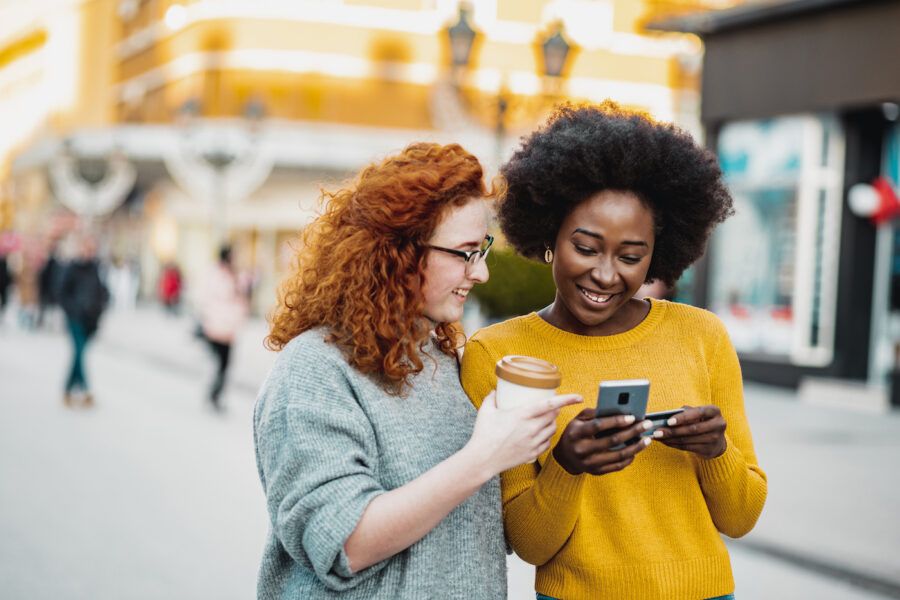 Photo of two female friends on the street holding smart phone and credit card