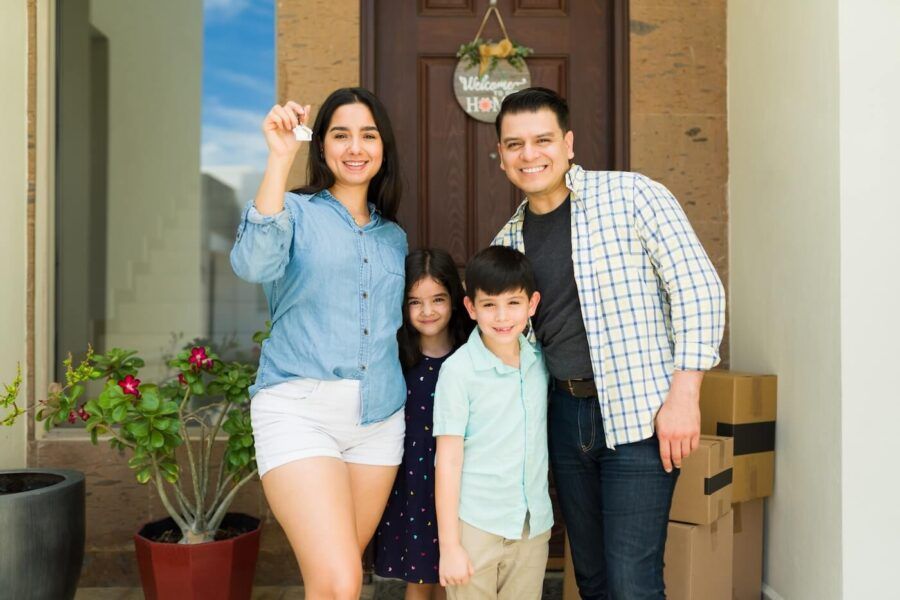 Happy family of four standing next to their new house and holding the keys