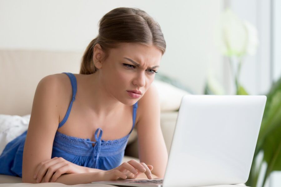 Confused young woman having problem with her email, looking at laptop screen with a frown.