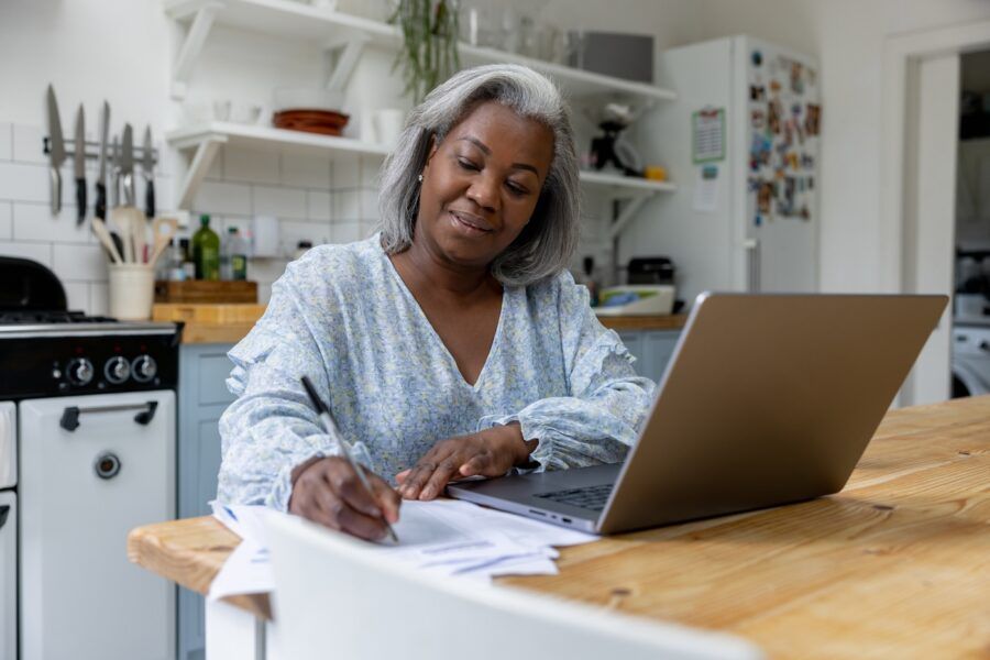 Mature woman at home doing taxes online using her laptop and writing some notes