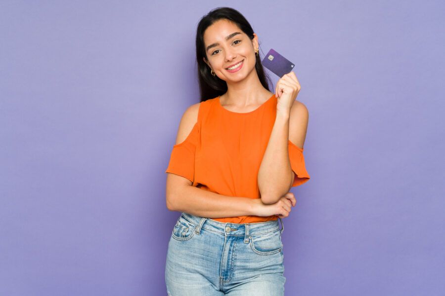 Smiling young woman holding a new debit card in front of a purple background.