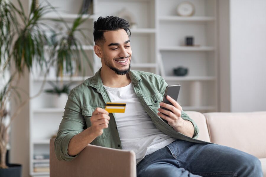 A man sitting on a couch holding his mobile phone and credit card.