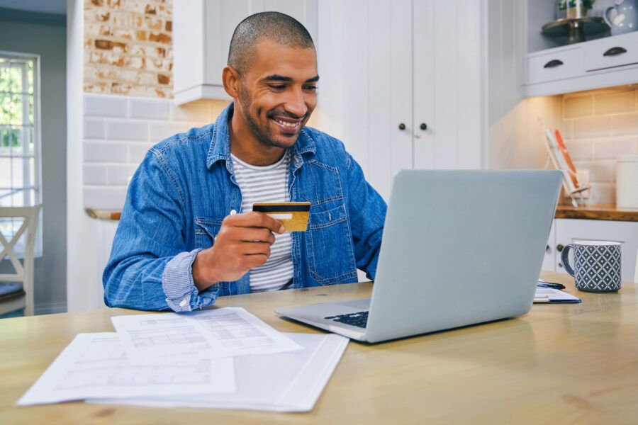 Shot of a young man using a laptop and credit card while working at home