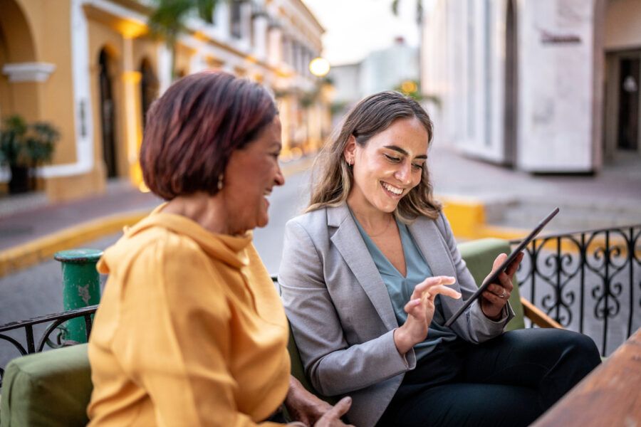 Two women having a meeting outside at a coffee shop, smiling and looking at a tablet