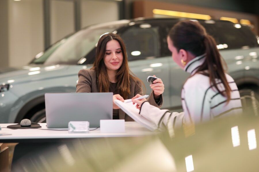 Female dealership agent taking a notepad from the female customer while giving her the car keys
