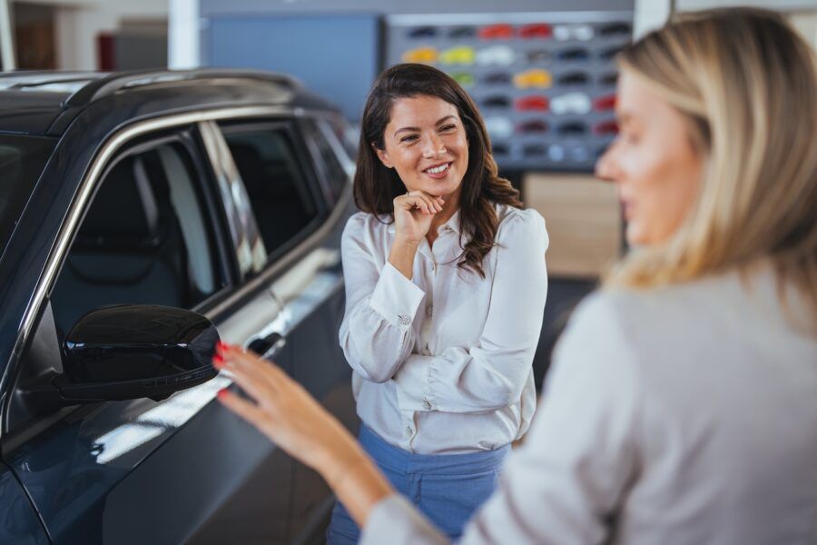 Businesswoman looking for a new car, standing next to a new SUV indoors at a car dealer.