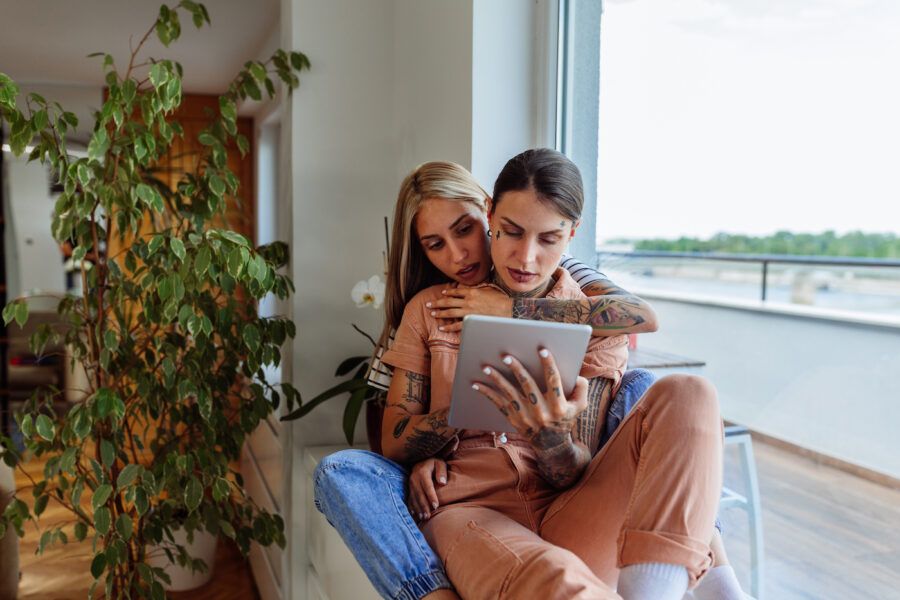 Loving female couple using digital tablet as they relax at home together