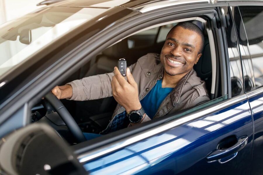 Excited young man sitting in the driver’s seat of a new blue car and holding up the key fob