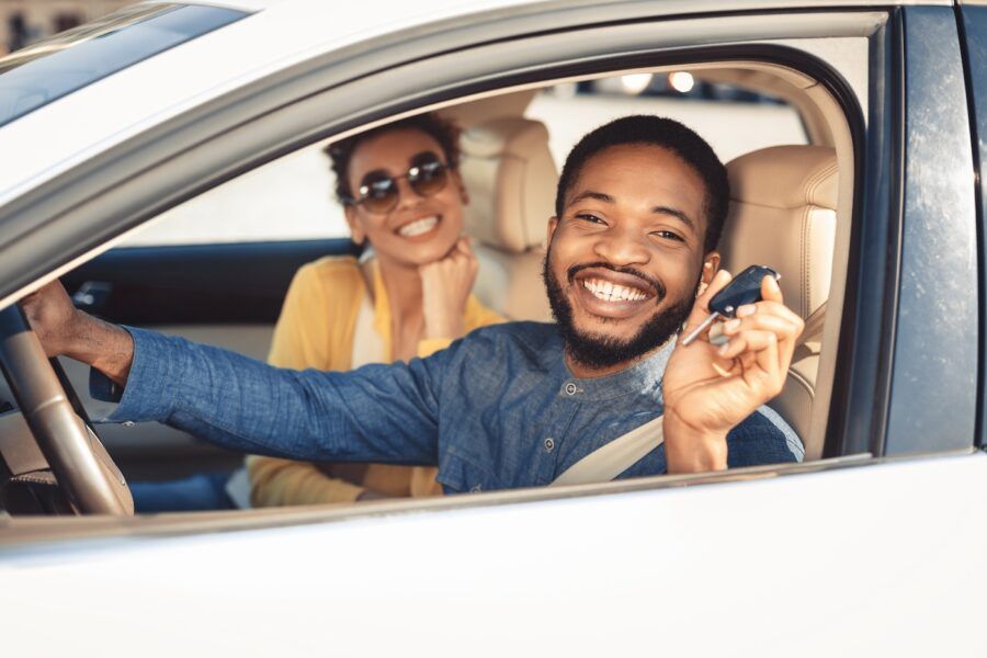 A happy couple showing car key, looking at camera and smiling, sitting in new car.