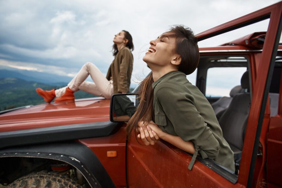 Cheerful women enjoying her active weekend with her friend while traveling in their off-road car