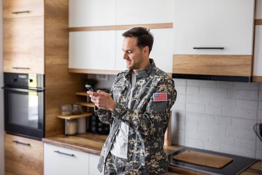 Smiling military man checking his phone in the kitchen