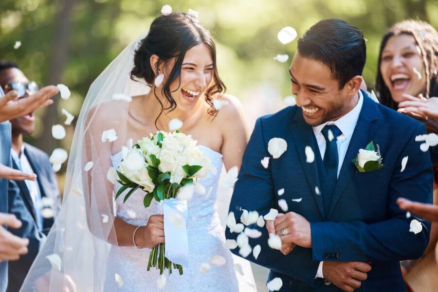 Happy newly married couple surrounded by guests who are throwing white petals in the air