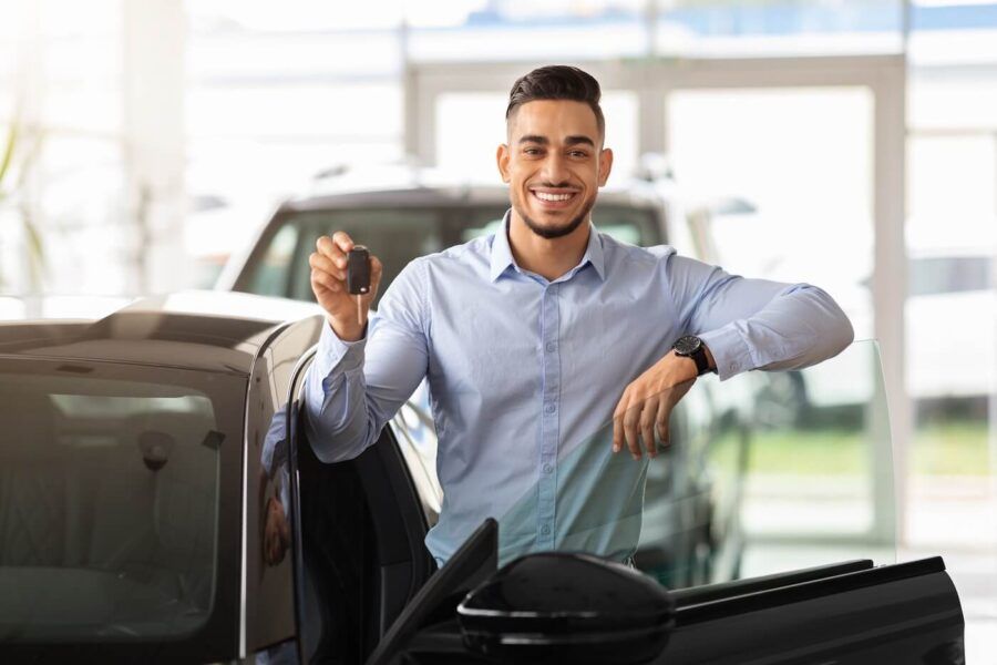 Smiling young man standing next to a new car and holding car keys