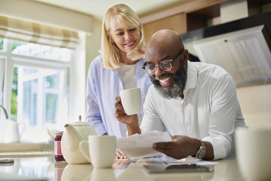 Couple reviewing financial documents while standing at their kitchen counter, smiling and drinking coffee