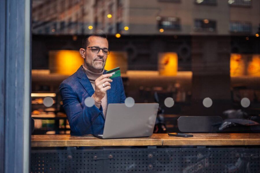 Mature businessman sitting in a cafe and making a wire transfer on his laptop