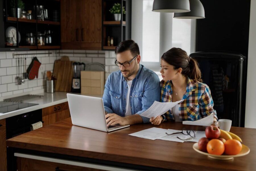 Focused young couple using the laptop and reviewing their bills in the kitchen