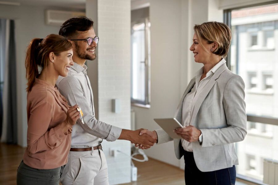 Happy young couple receiving new house keys and shaking hands with the female agent