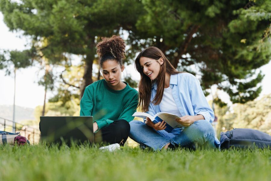 Two female students working and learning together sitting on University campus grass
