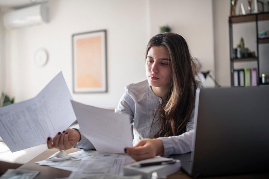 Focused young woman reviewing her bills while using a laptop at home