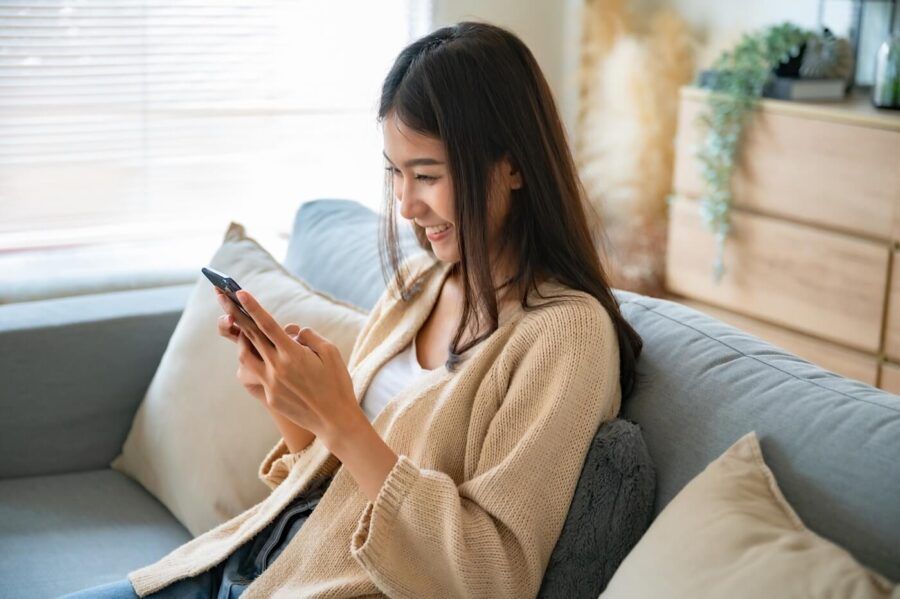 Smiling young woman sitting on a sofa and using her smatphone