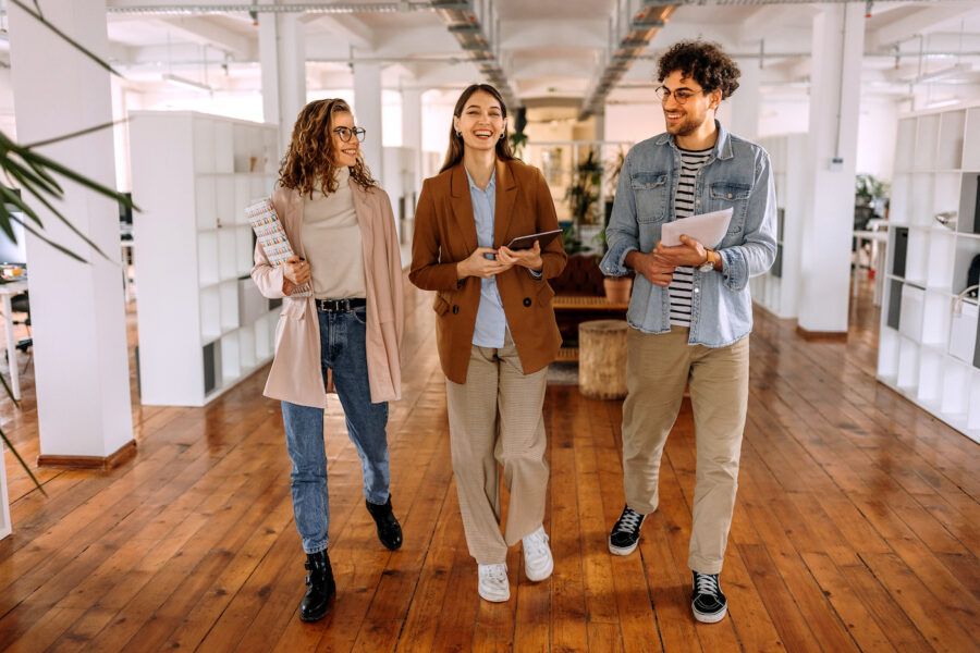 Group of smiling young colleagues walking and talking in modern office
