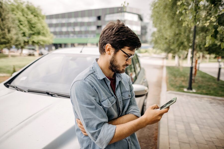 Young man using phone in front of the car