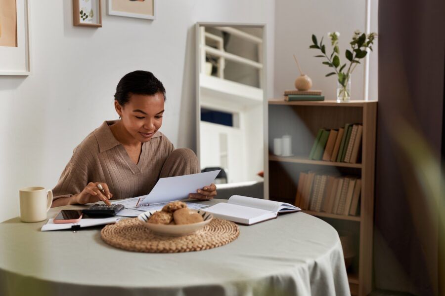 A portrait of smiling young woman reading finance paperwork at home.