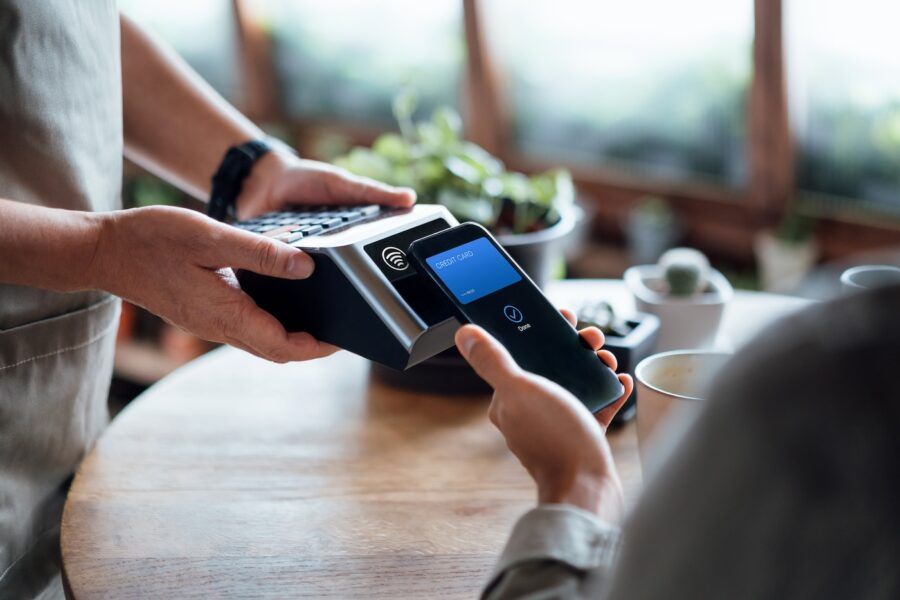 Close up of a male's hand paying bill with contactless payment on smartphone in a cafe, scanning on a card machine.