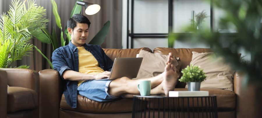 A man relaxing on the couch with his laptop, checking his bank account.
