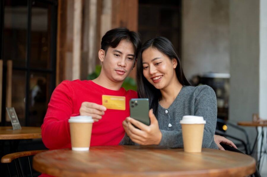 Smiling young couple enjoying coffee at a café while using a mobile app to make a credit card transaction