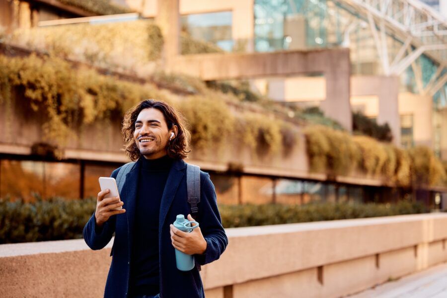 Happy man using earbuds and cell phone walking outdoors.
