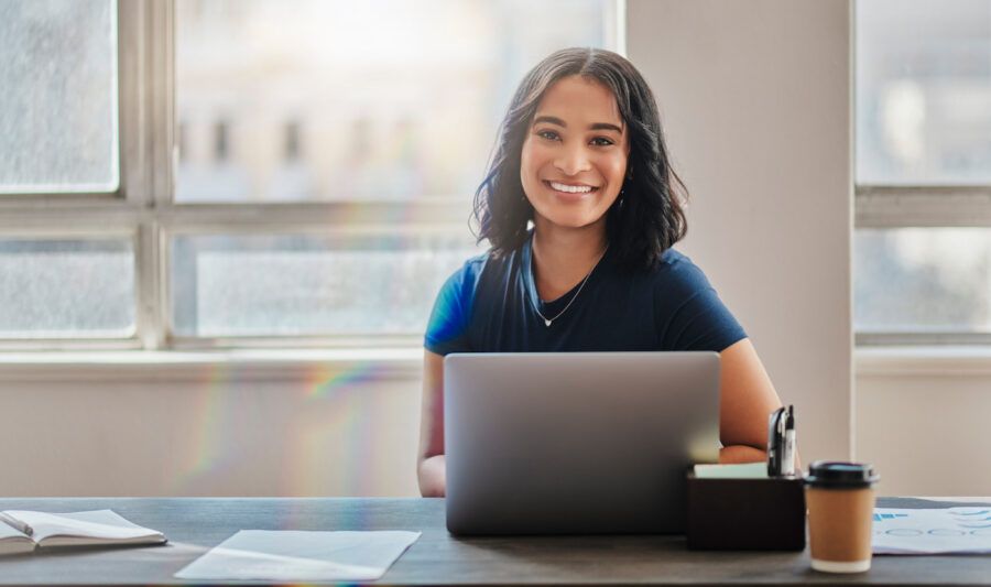 A woman smiling and working on laptop in office.