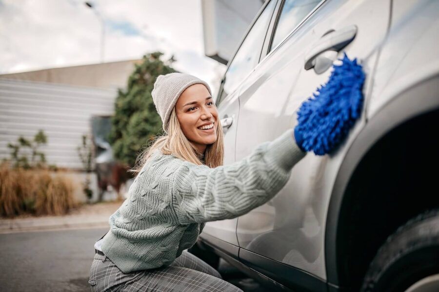 Smiling young woman wiping her car with a sponge glove