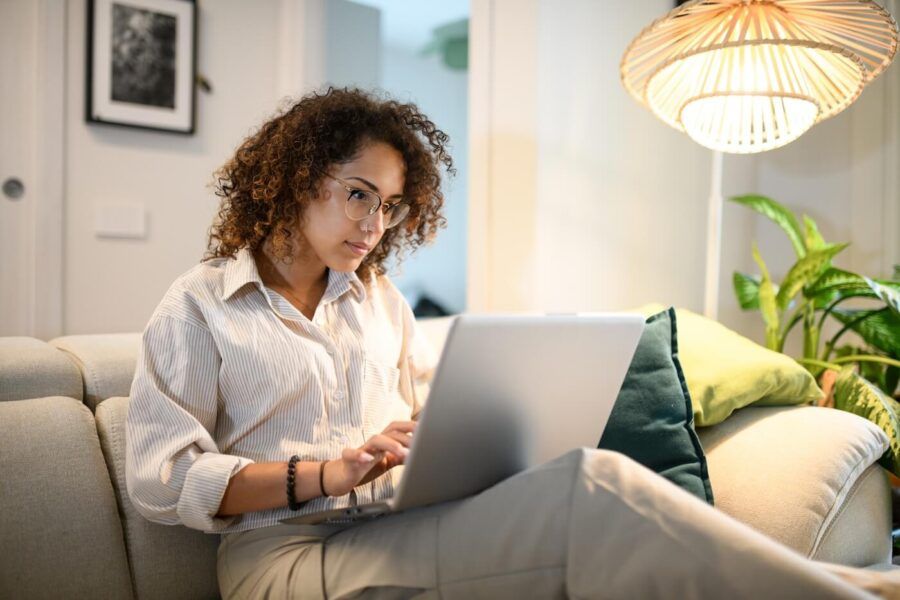 Focused woman using her laptop to open a bank account online while sitting on the sofa in the cozy living room